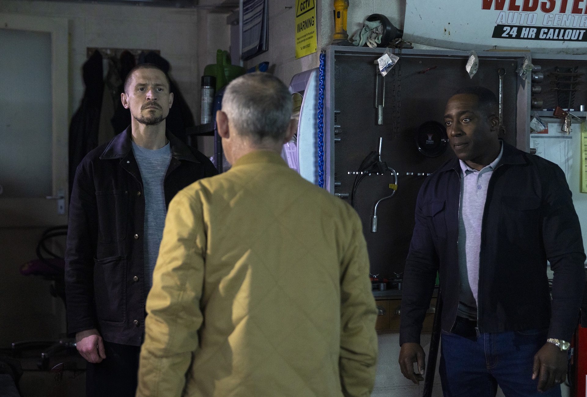 Carl, Kevin and Ronnie serious in the garage in Coronation Street